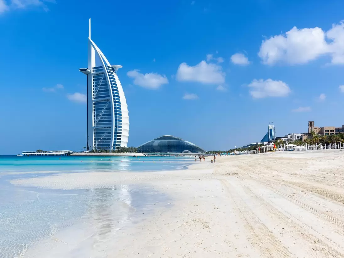 A sail-shaped hotel standing offshore beyond a wide empty beach.