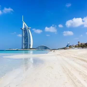 A sail-shaped hotel standing offshore beyond a wide empty beach.