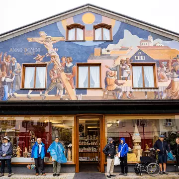Tourists hide from the rain under the awning of a building with a painted fresco of the village's historic Passion Play