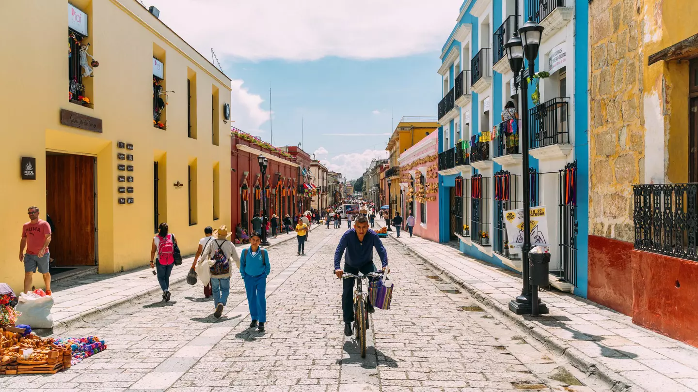People walking, cycling and selling souvenirs on a colorful pedestrian stree in Oaxaca