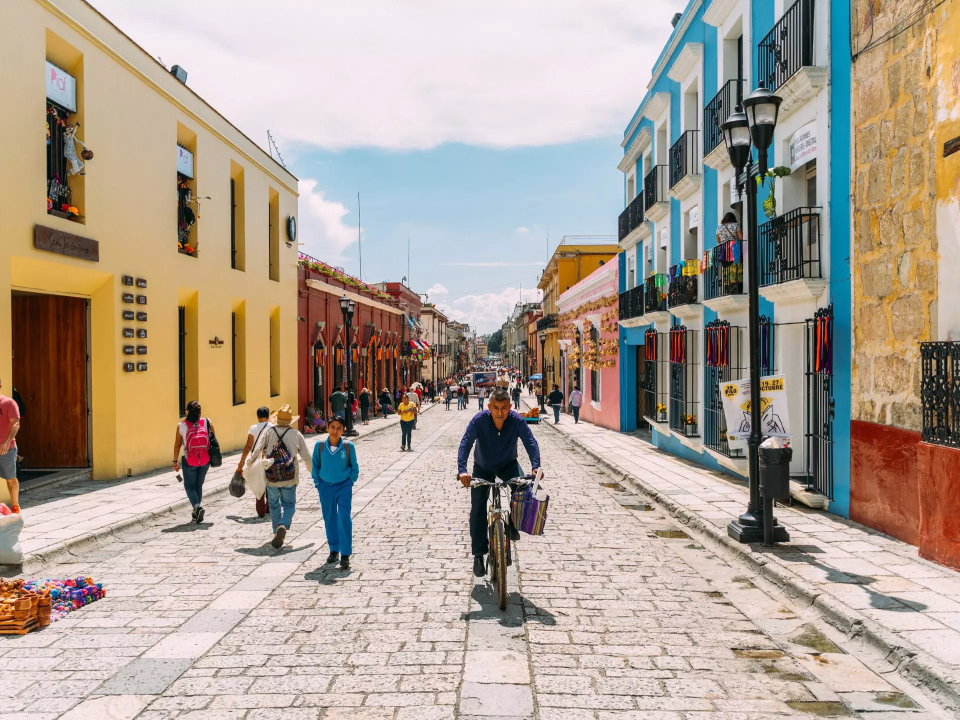People walking, cycling and selling souvenirs on a colorful pedestrian stree in Oaxaca