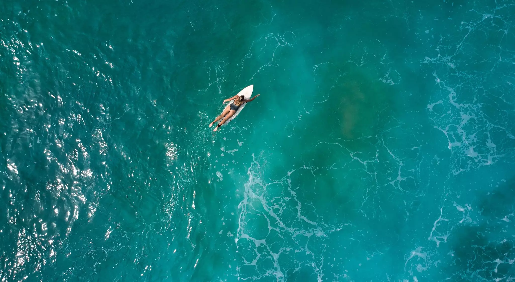 A surfer in the ocean paddles along on her surfboard.