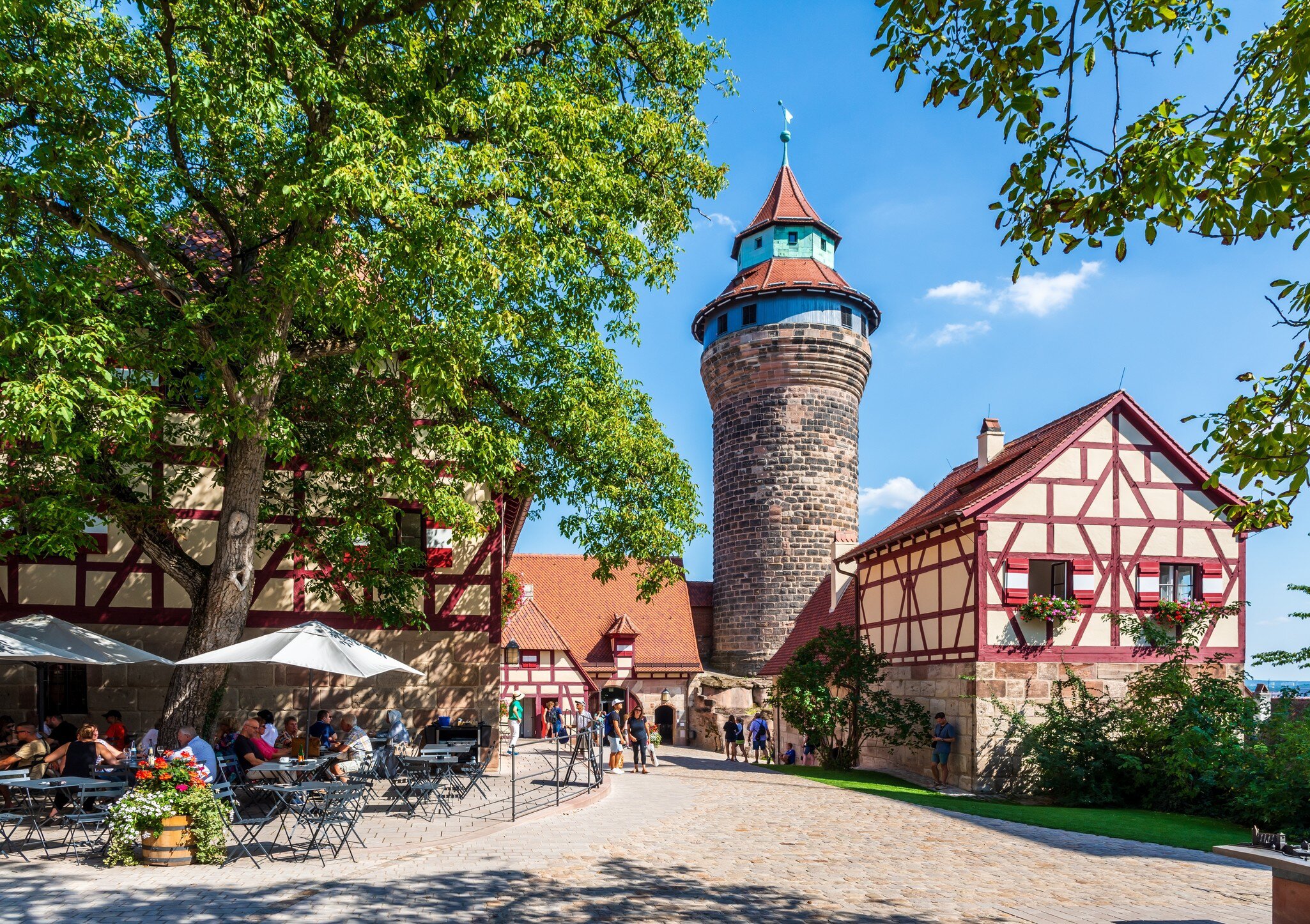 Tourists in the courtyard of the Kaiserburg medieval castle with the Tiefer Brunnen (well) in the Brunnenhaus half-timbered house and the Sinwellturm (keep). Nuremberg, Germany.