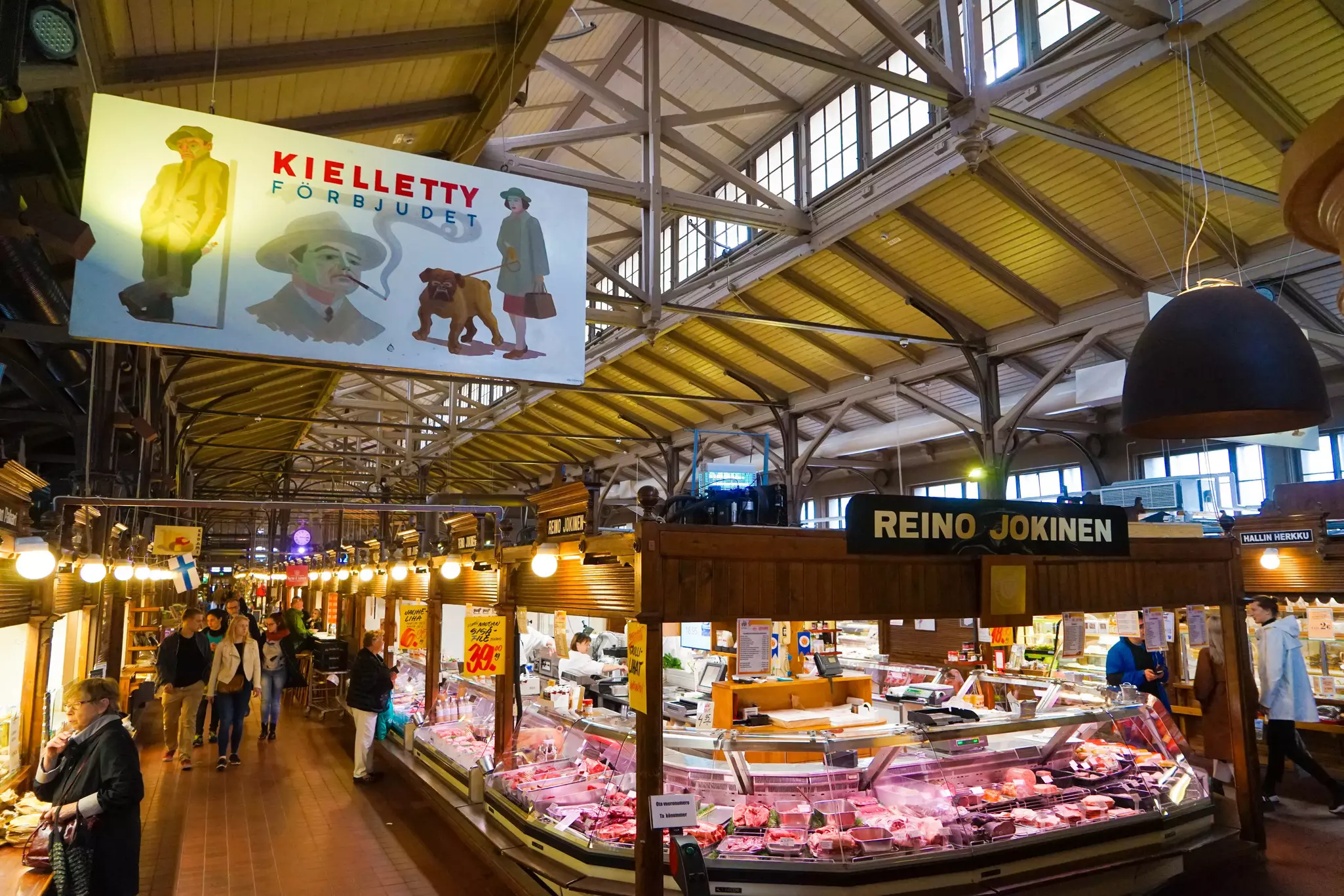 The interior of Turku Market Hall. Several vendors have stalls selling food in the vast space, and many shoppers are browsing.