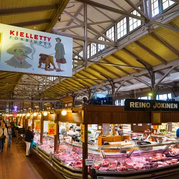 A butcher stall displays meant under the tall ceiling of a covered market hall.