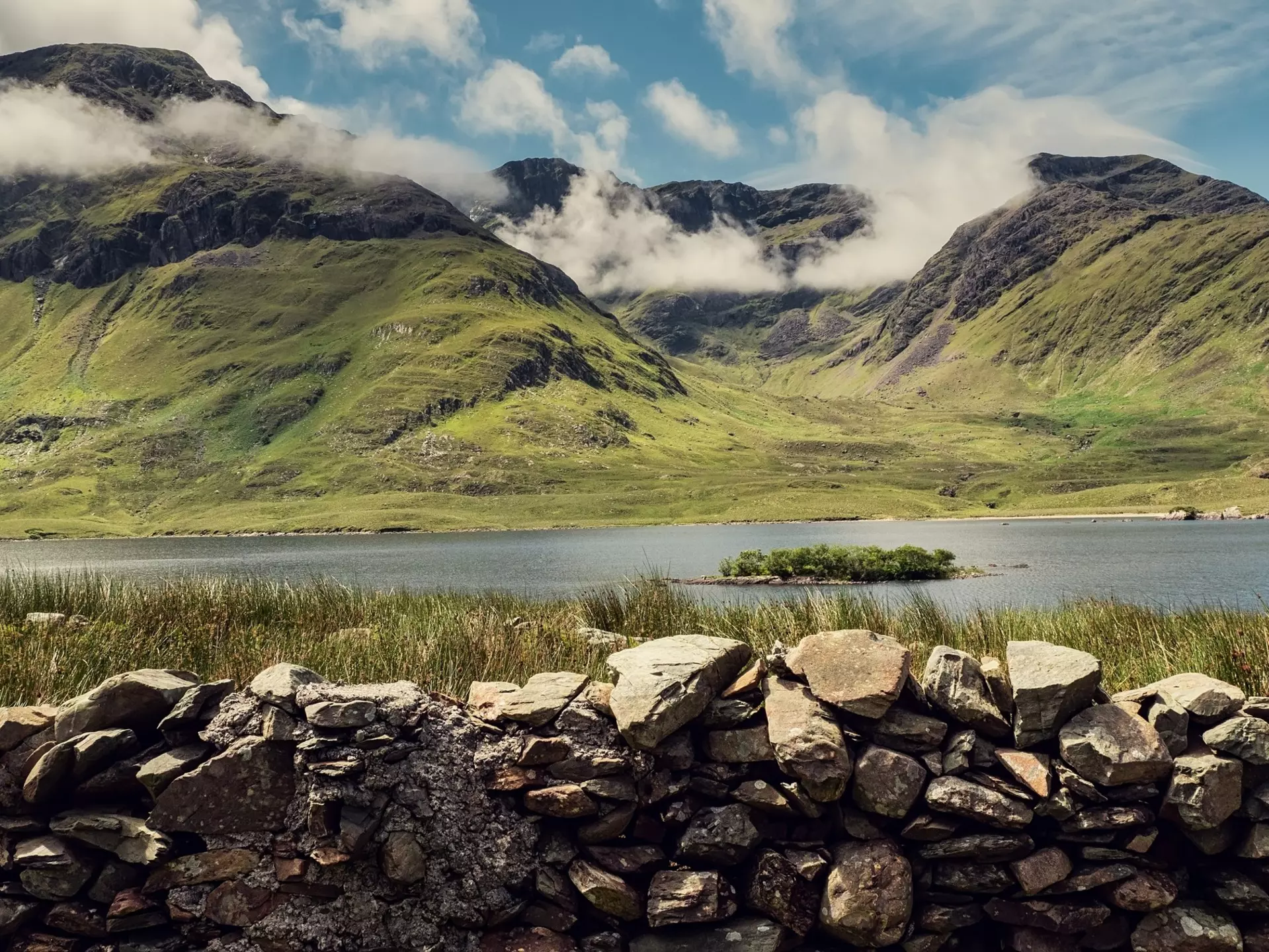 Clouds hug rocky mountains seen beyond a lake fronted by rocks in Connemara, Ireland