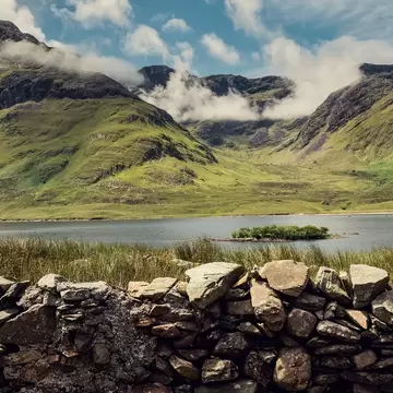 Clouds hug rocky mountains seen beyond a lake fronted by rocks in Connemara, Ireland