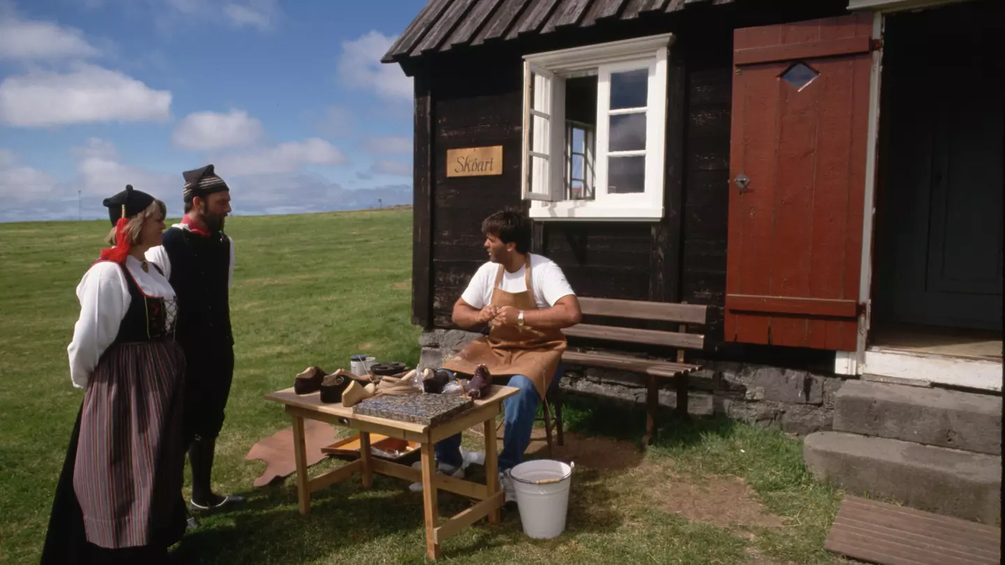 Wearing traditional dress, actors at Arbaejarsafn, or Open Air Museum, talk to a fellow actor at his shoemaking post. Reykjavik, Iceland