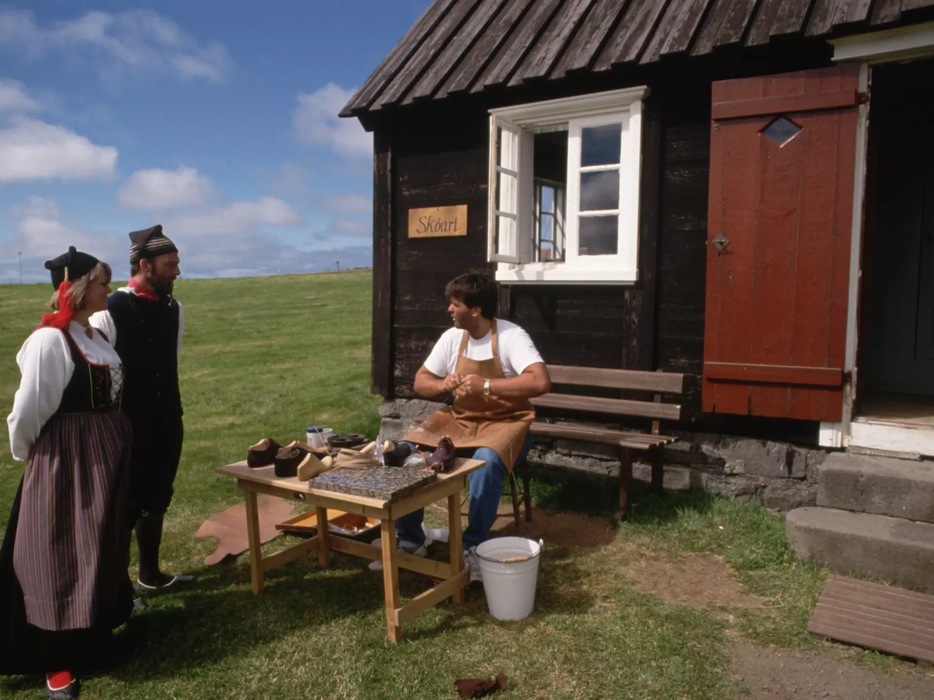 Wearing traditional dress, actors at Arbaejarsafn, or Open Air Museum, talk to a fellow actor at his shoemaking post. Reykjavik, Iceland