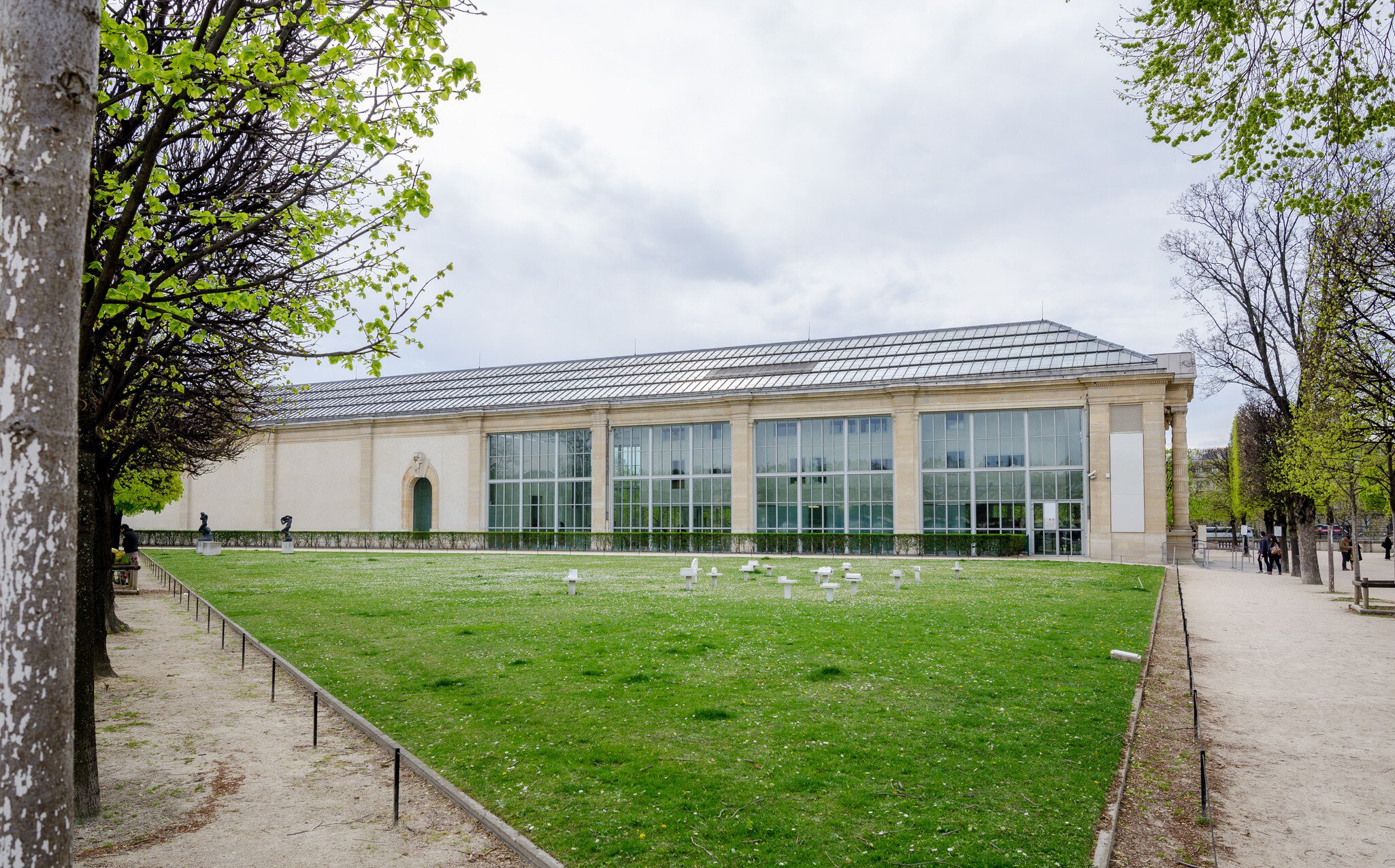 Exterior of the Musée de l’Orangerie (Oragnery Museum) in the Tuileries Gardens in Paris, France, on a cloudy day. Green grass and trees surrounding.