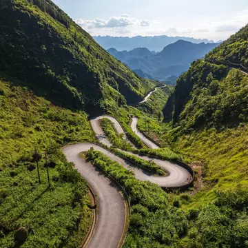 A series of switchbacks on a road through a mountain pass are seen from above.