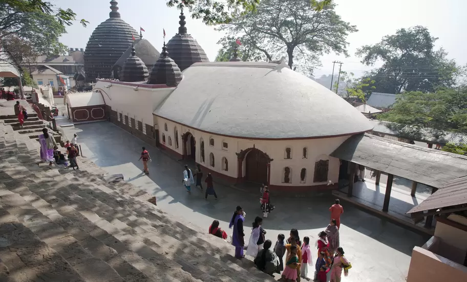 Kamakhya Temple in Guwahati, Assam, with beehive-shaped domes and a whitewashed hall, pilgrims on stone steps in front