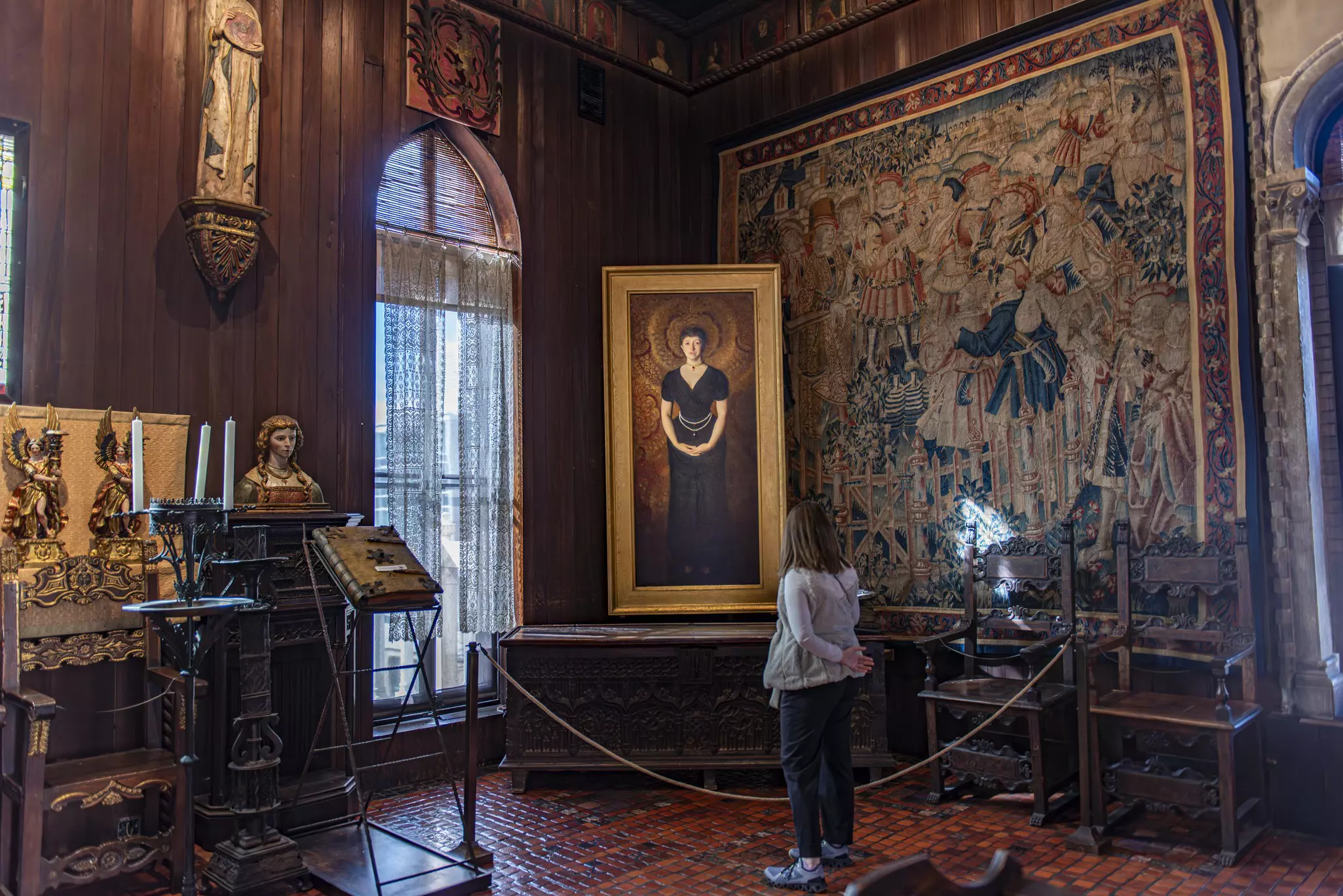 A gallerygoer looks at a painted portrait of woman in a museum gallery, which also contains sculptures, tapestries and other artworks.