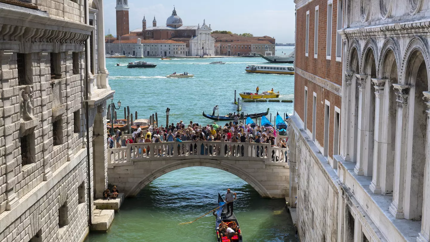 A gondola travels under the crowded Ponte della Paglia bridge in Venice