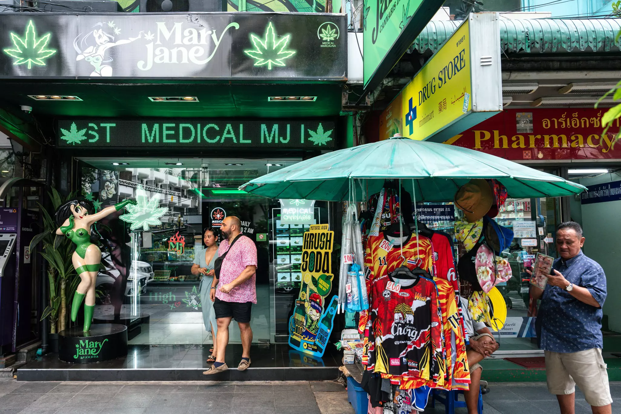 People leave a marijuana dispensary on a crowded city street with street vendors out front.