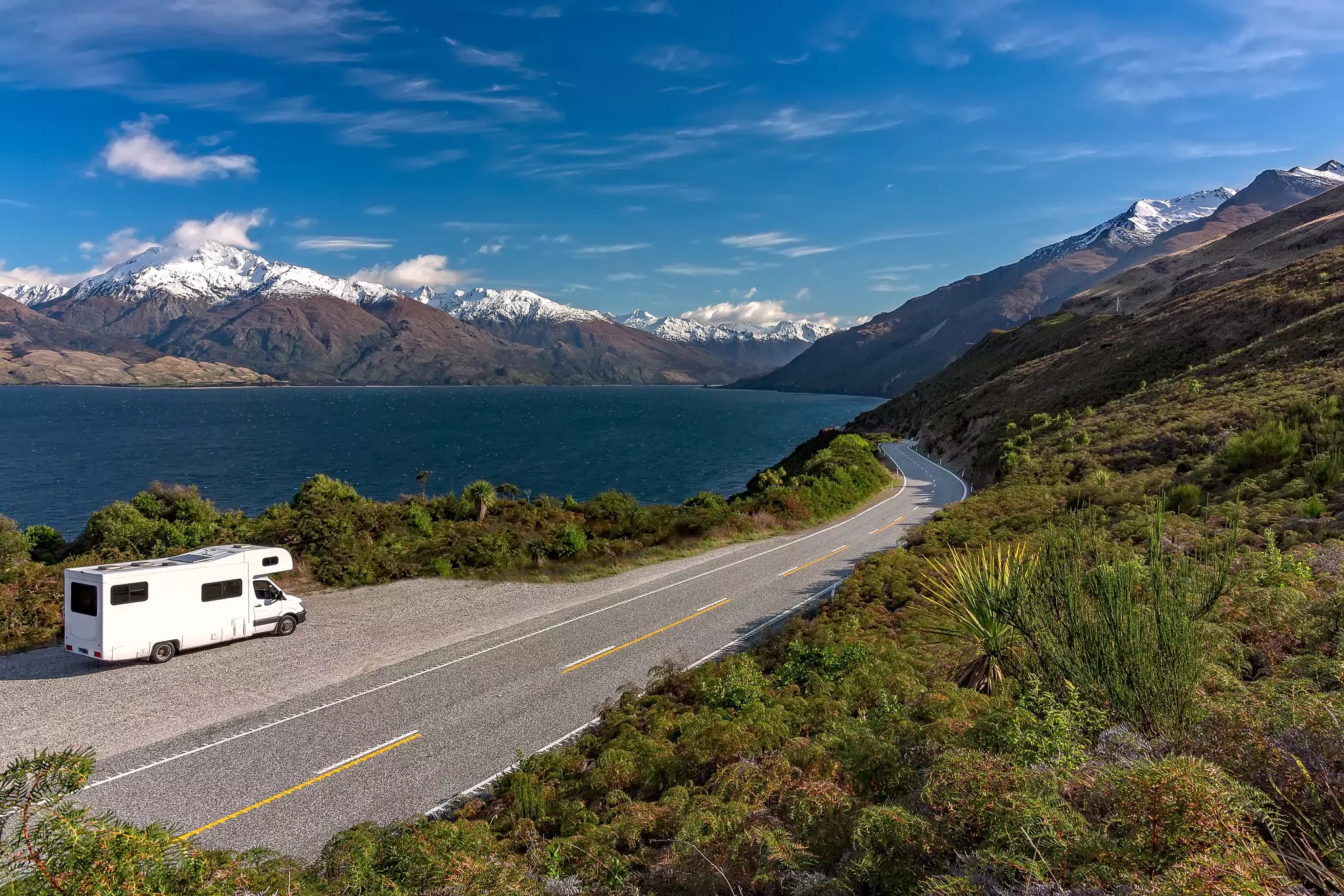 A white camper-van parked in a lay-by viewpoint on the banks of Lake Wānaka with dramatic snow capped peaks in the distance, Queenstown NZ