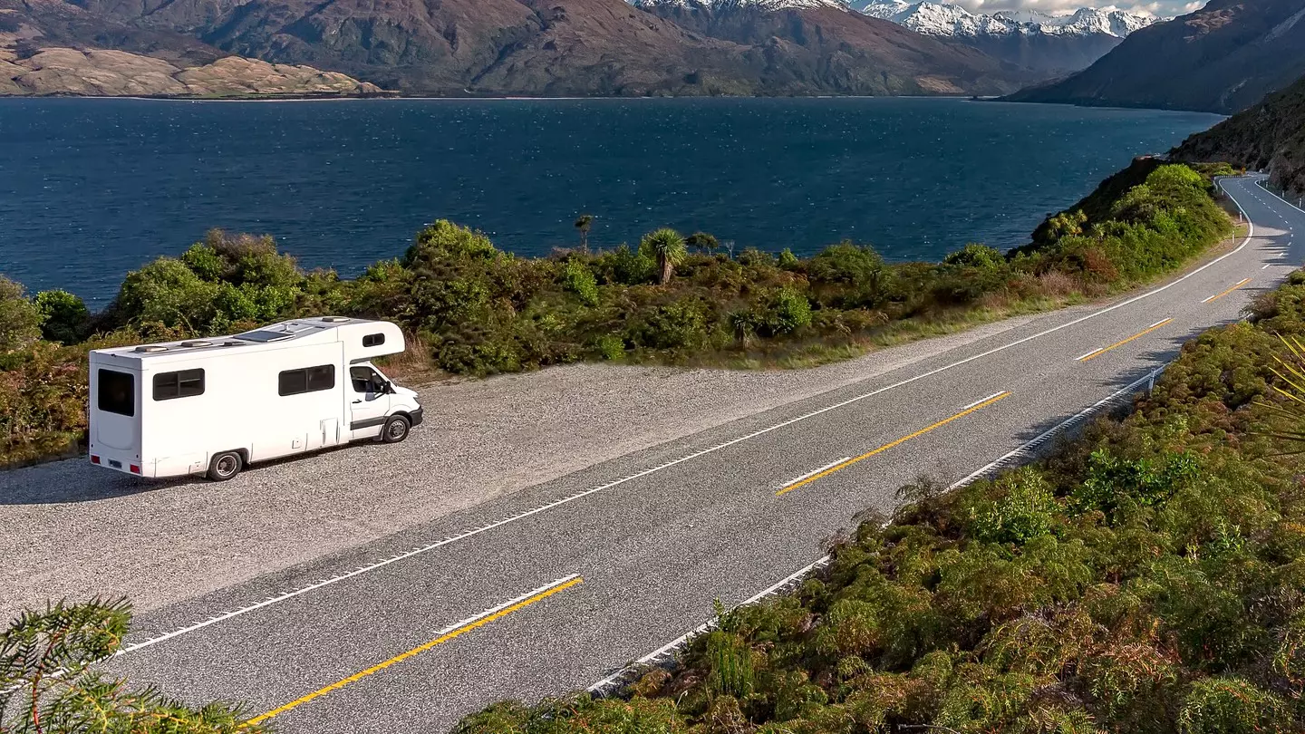 A white camper-van parked in a lay-by viewpoint on the banks of Lake Wānaka with dramatic snow capped peaks in the distance, Queenstown NZ