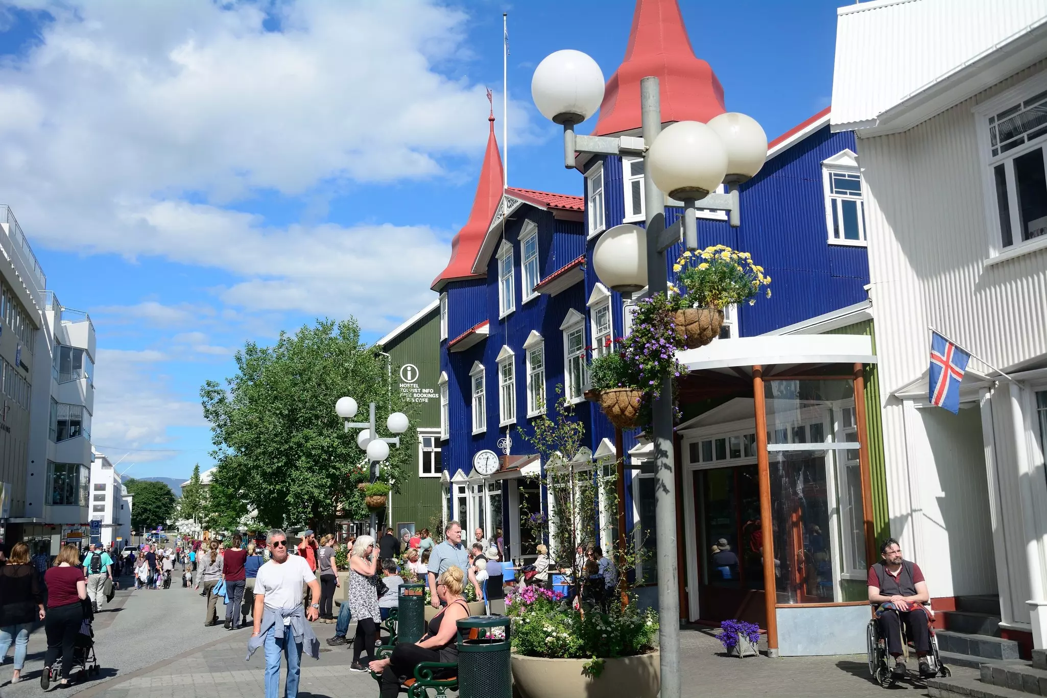 People walk down a pedestrianized street in a city in summer. A building is painted deep blue.