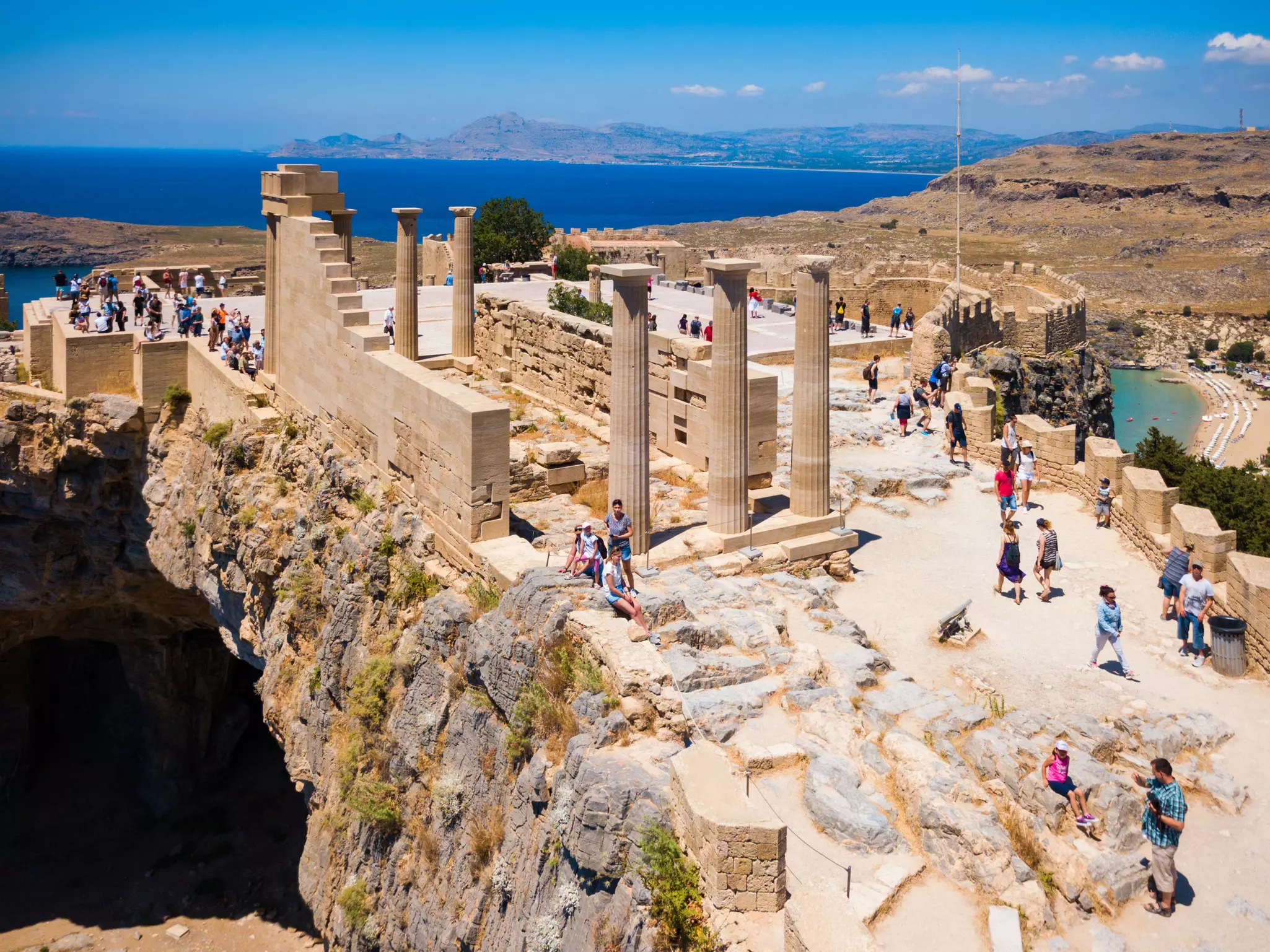 Many visitors at an archaeological site of coastal Greek ruins.