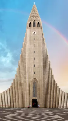 A tall church tower with a rainbow to the side.
