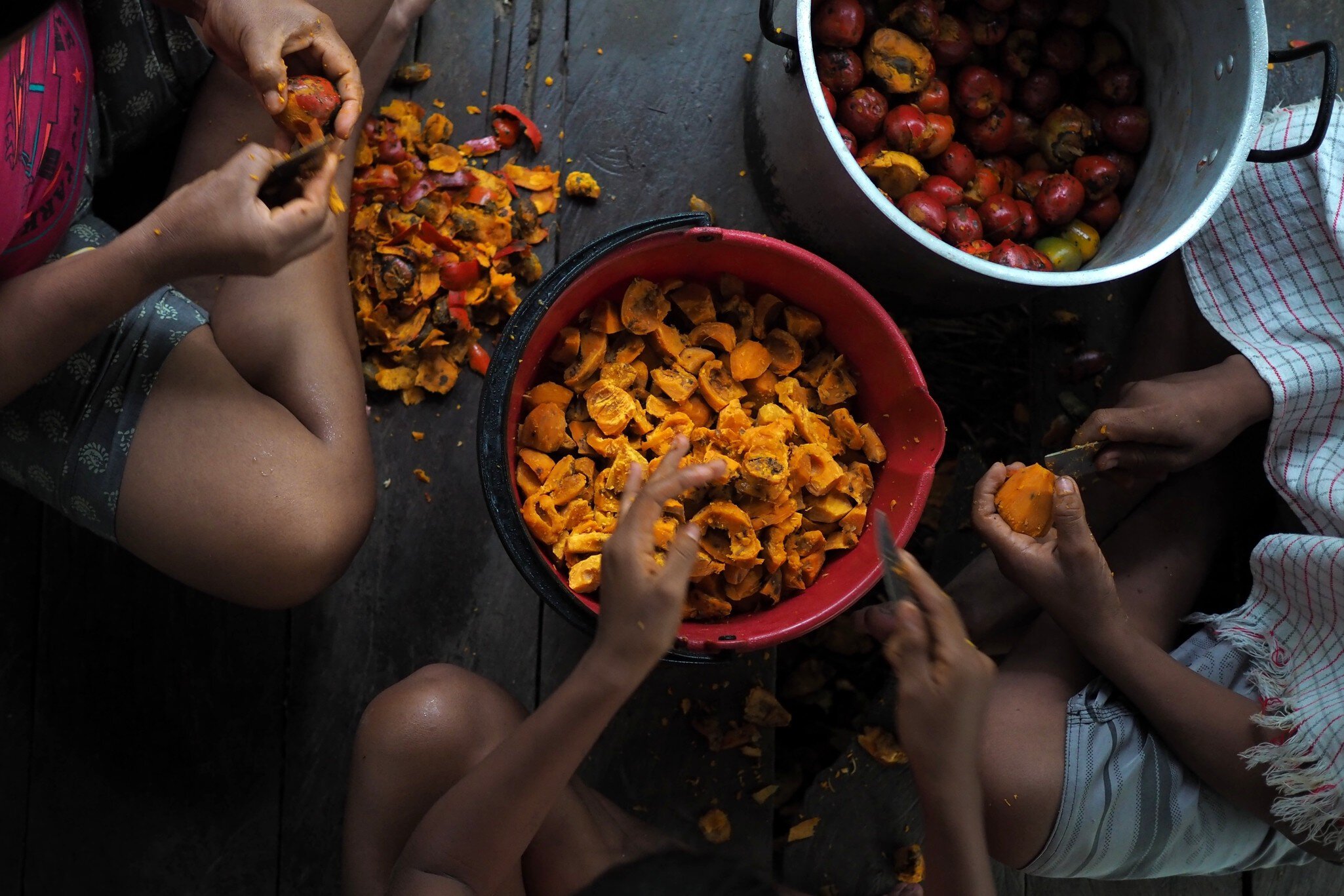 Children skinning fruits on the floor of a kitchen in Leticia.
