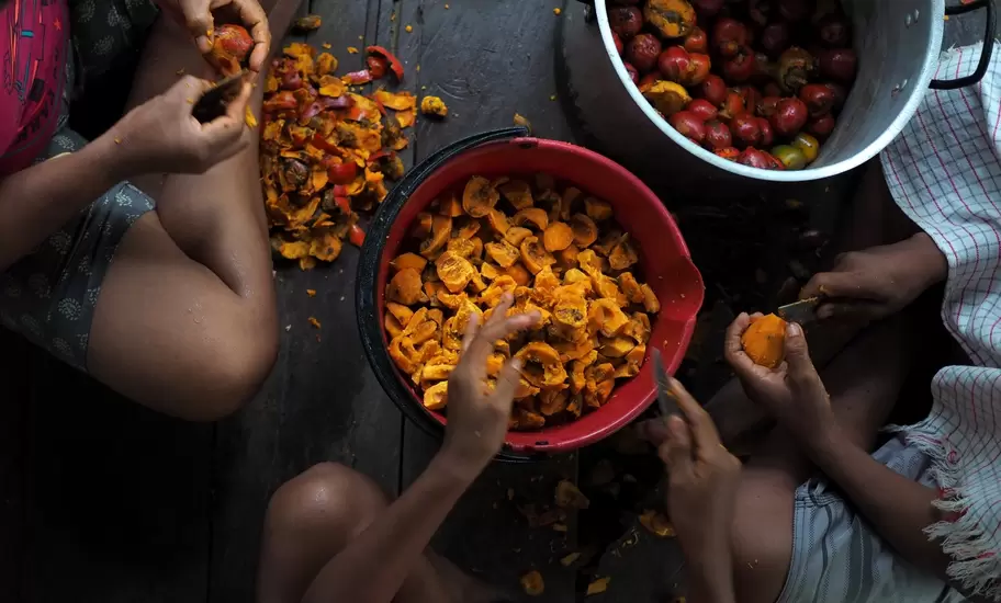 Children skinning fruits on the floor of a kitchen in Leticia.