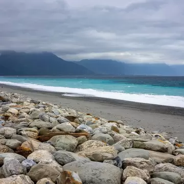 Pebble beach at Qixingtan in Hualien with rough turquoise surf and cloud-capped coastal mountains under grey skies