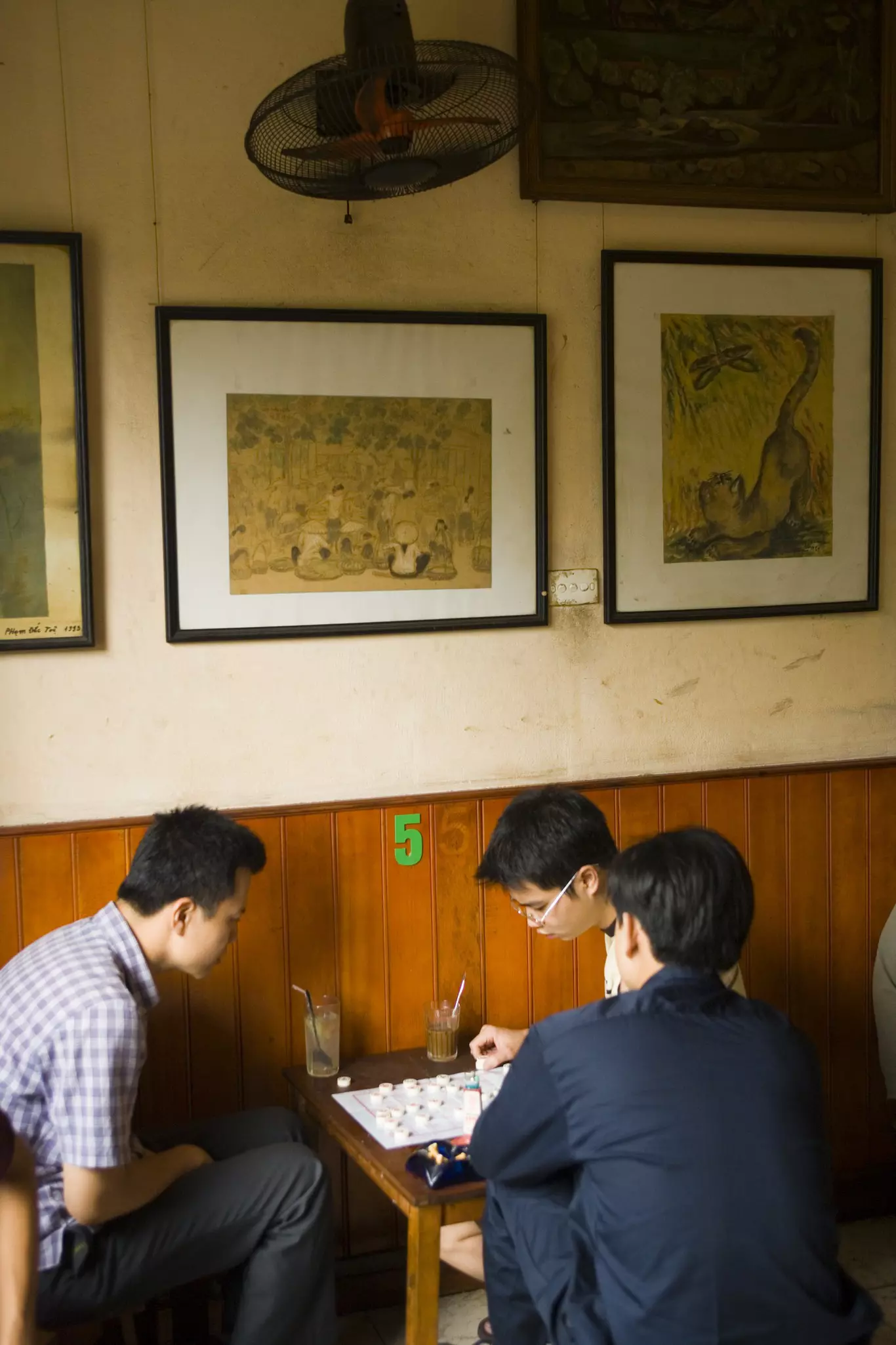 Three young men play a game on a low table in a cafe.
