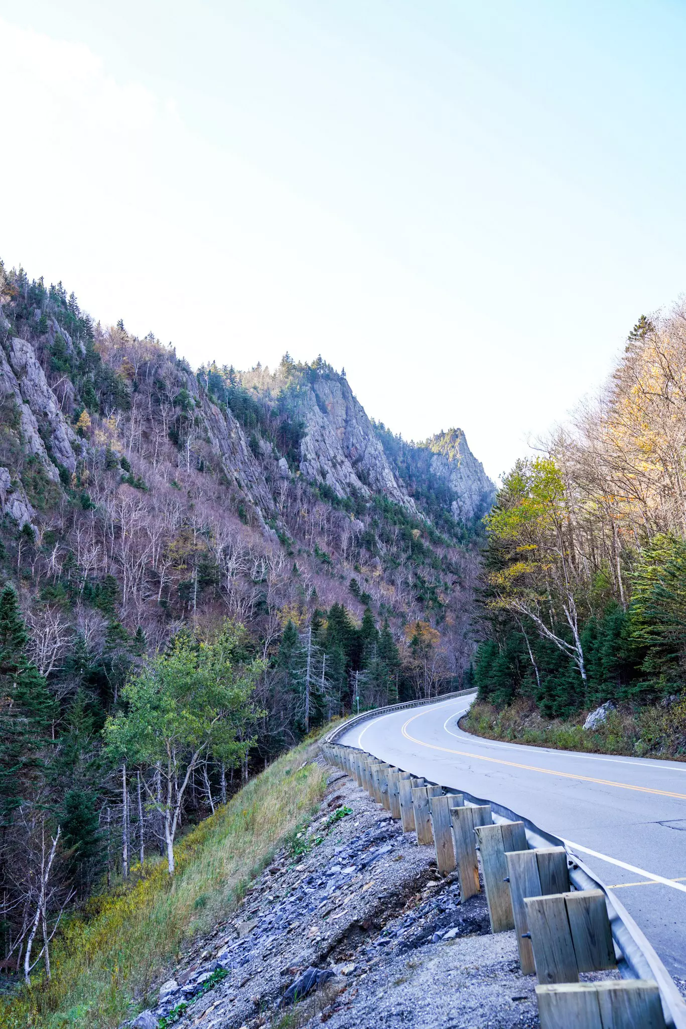 An empty two-lane blacktop road winds through a mountainous area of New Hampshire.