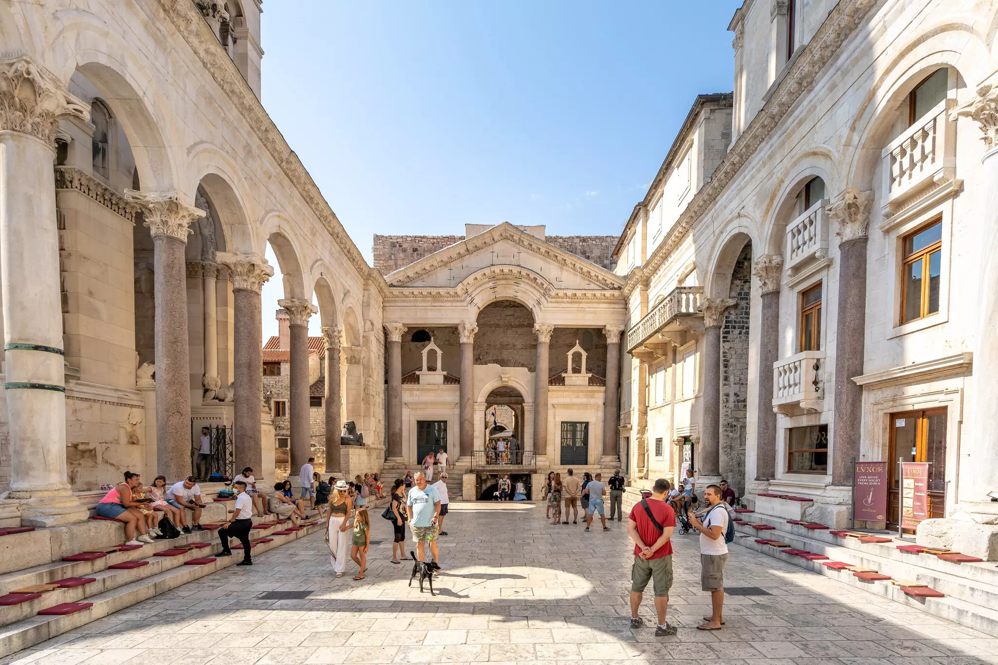 Tourists chat in a courtyard surrounded by ancient marble buildings