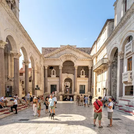 Tourists chat in a courtyard surrounded by ancient marble buildings