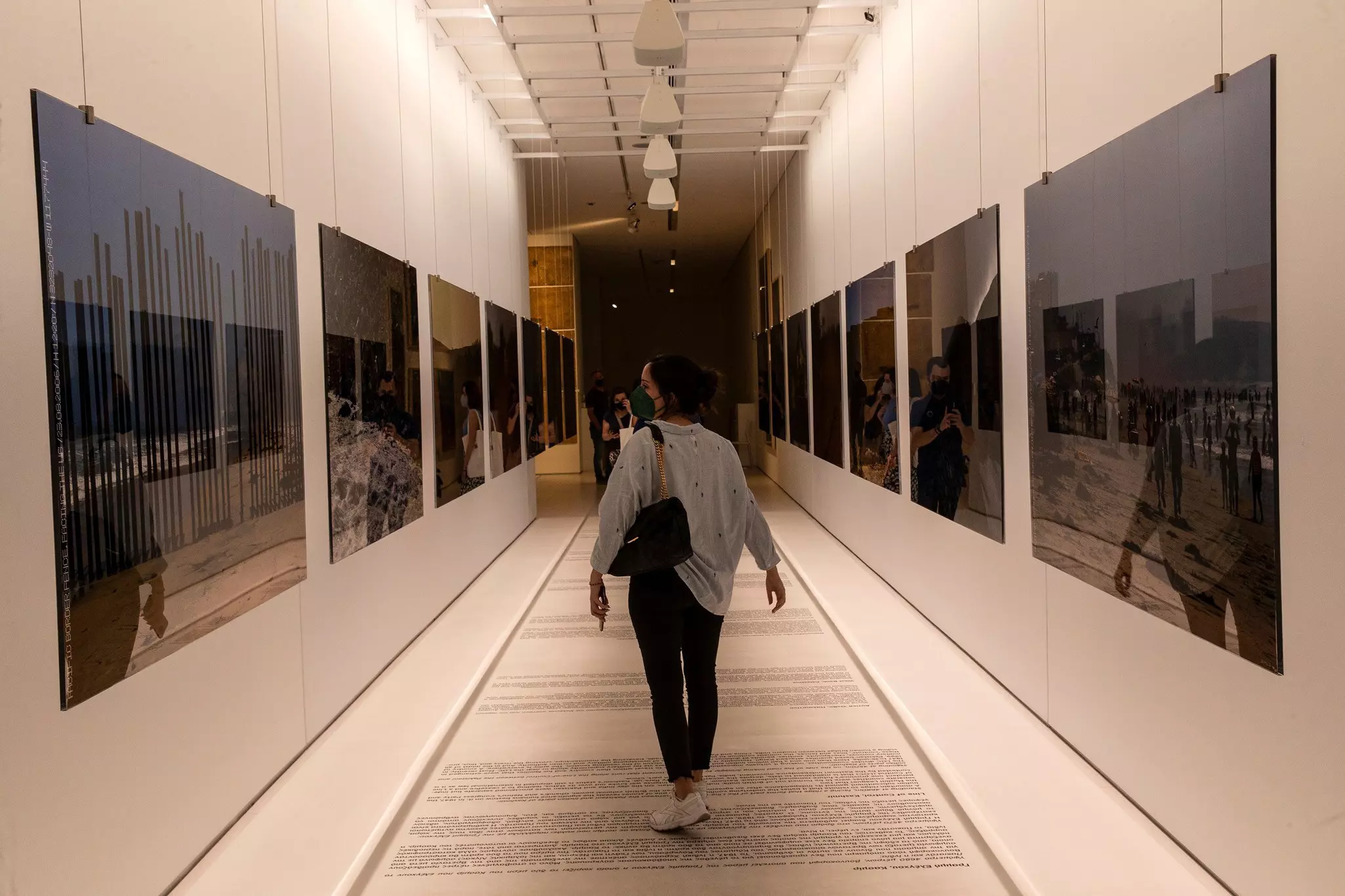 A woman wearing a face mask looks at artworks on the walls of a narrow gallery at a museum.