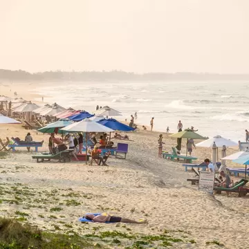 People under sunshades on a busy beach with waves crashing on the shore.