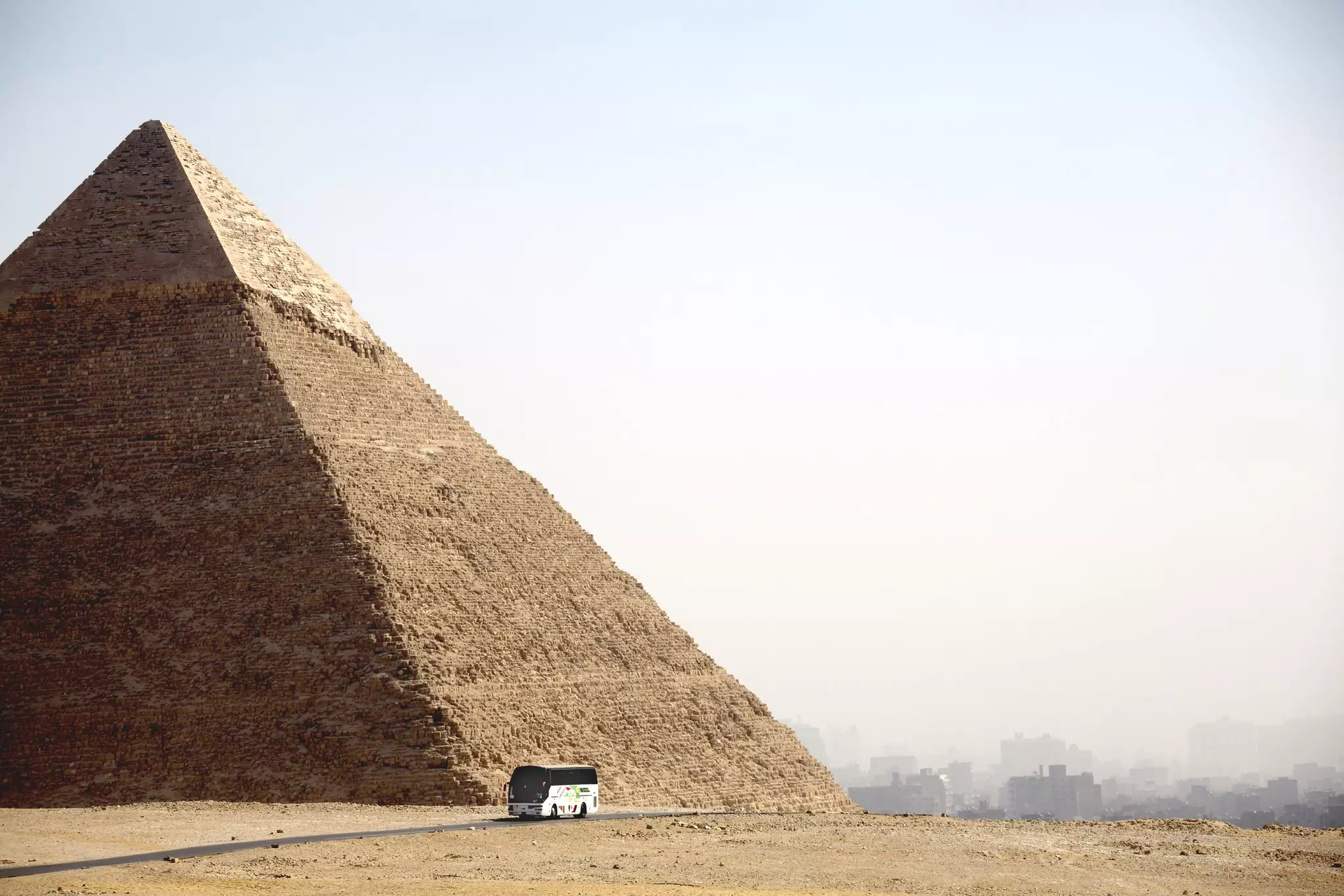 A bus drives past a vast stone pyramid in a dusty environment