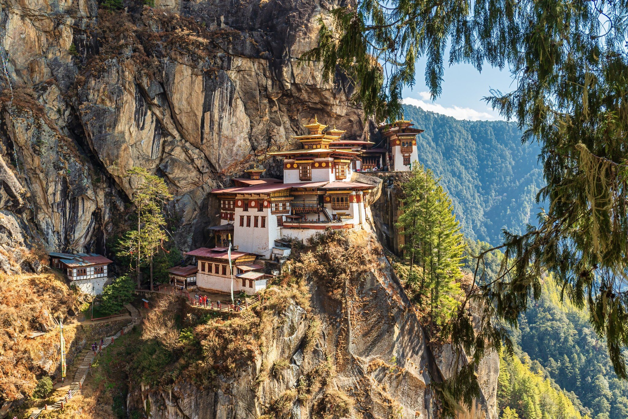 A whitewashed monastery clinging to a sheer cliff face above a forested gorge.