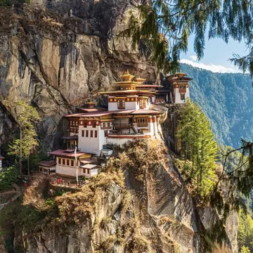A whitewashed monastery clinging to a sheer cliff face above a forested gorge.
