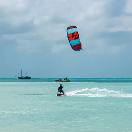 A person rides a kiteboard in turquoise water.