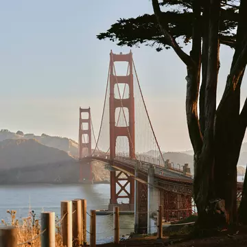 A red suspension bridge in late afternoon light from a shadowed landing.