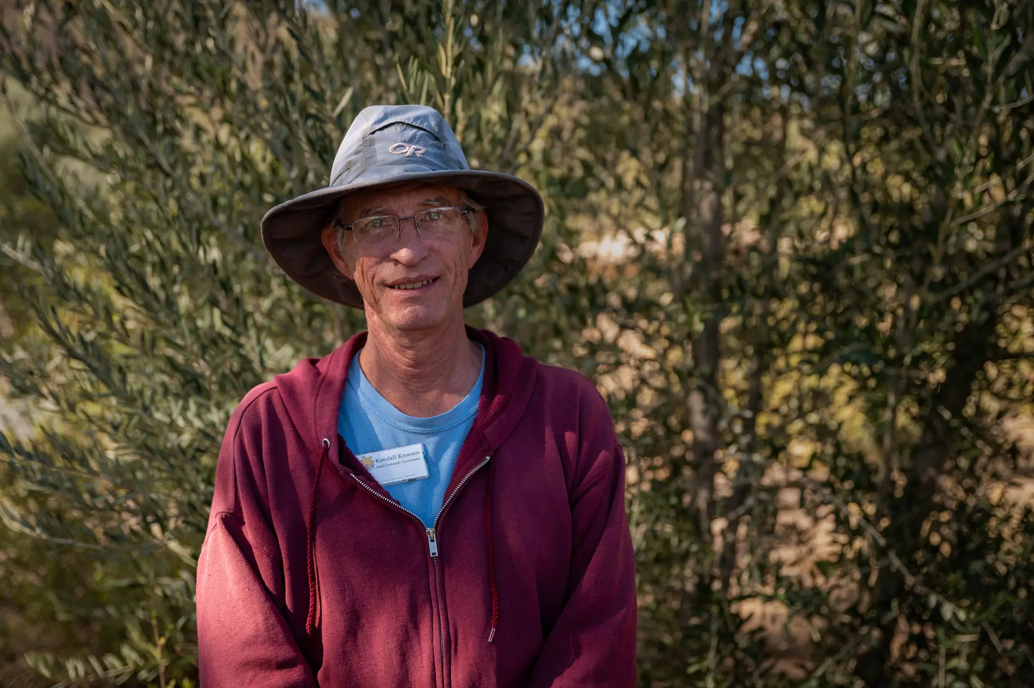 A man stands by a bush smiling at the camera