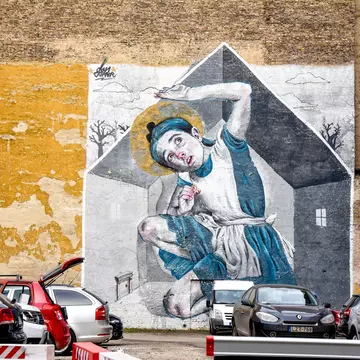 A mural of a young girl filling the space of a house whilst eating a cookie. She reaches above her head as it touches the ceiling of the house.