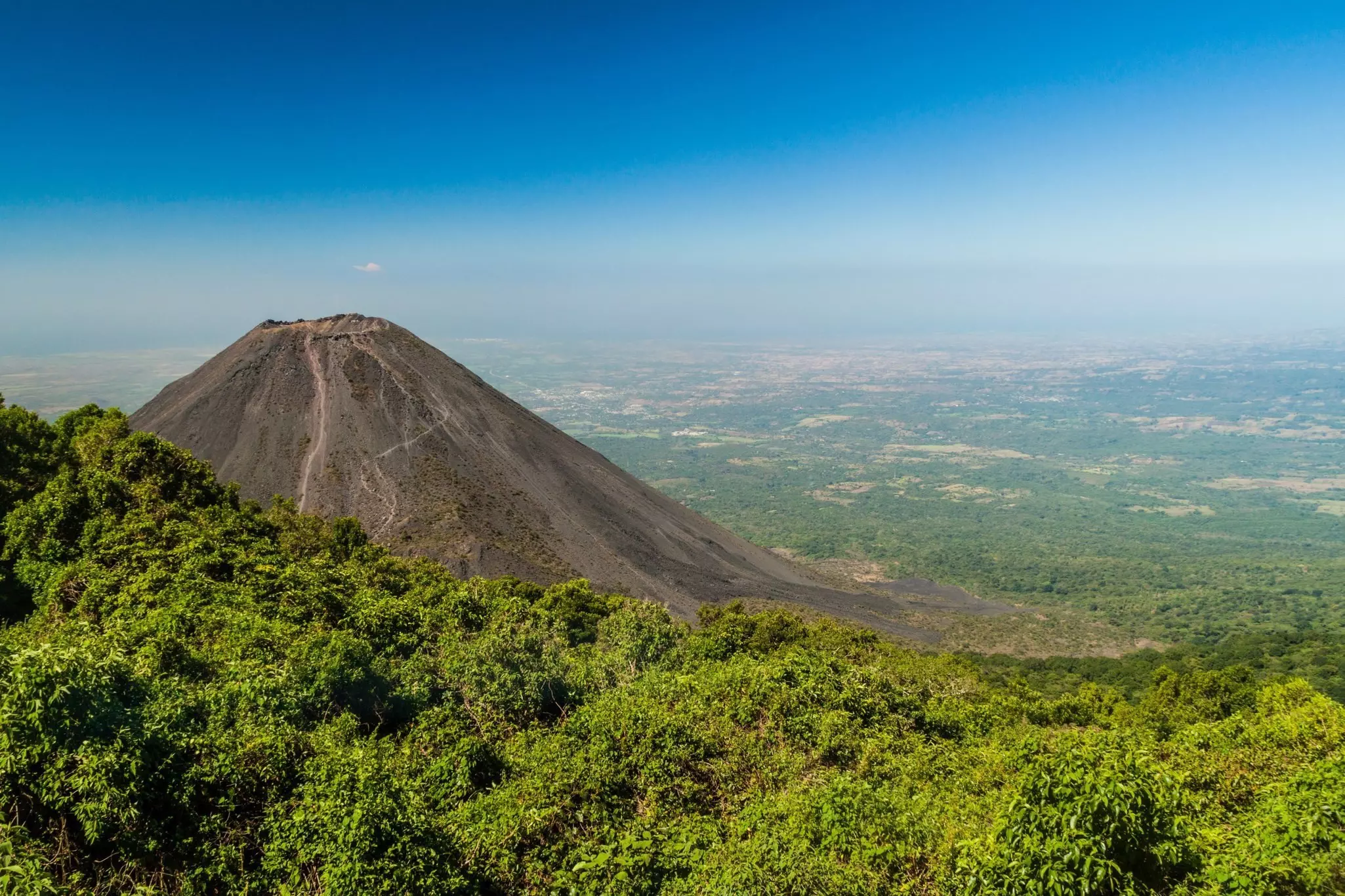 The cinder cone of a volcano juts from its green surroundings
