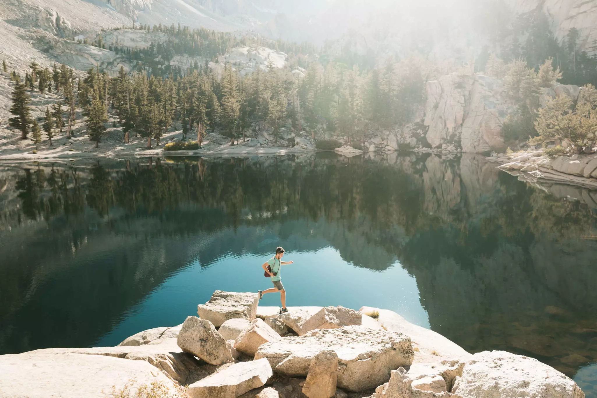 A young sporty man runs and jumps on the rocks next to a lake