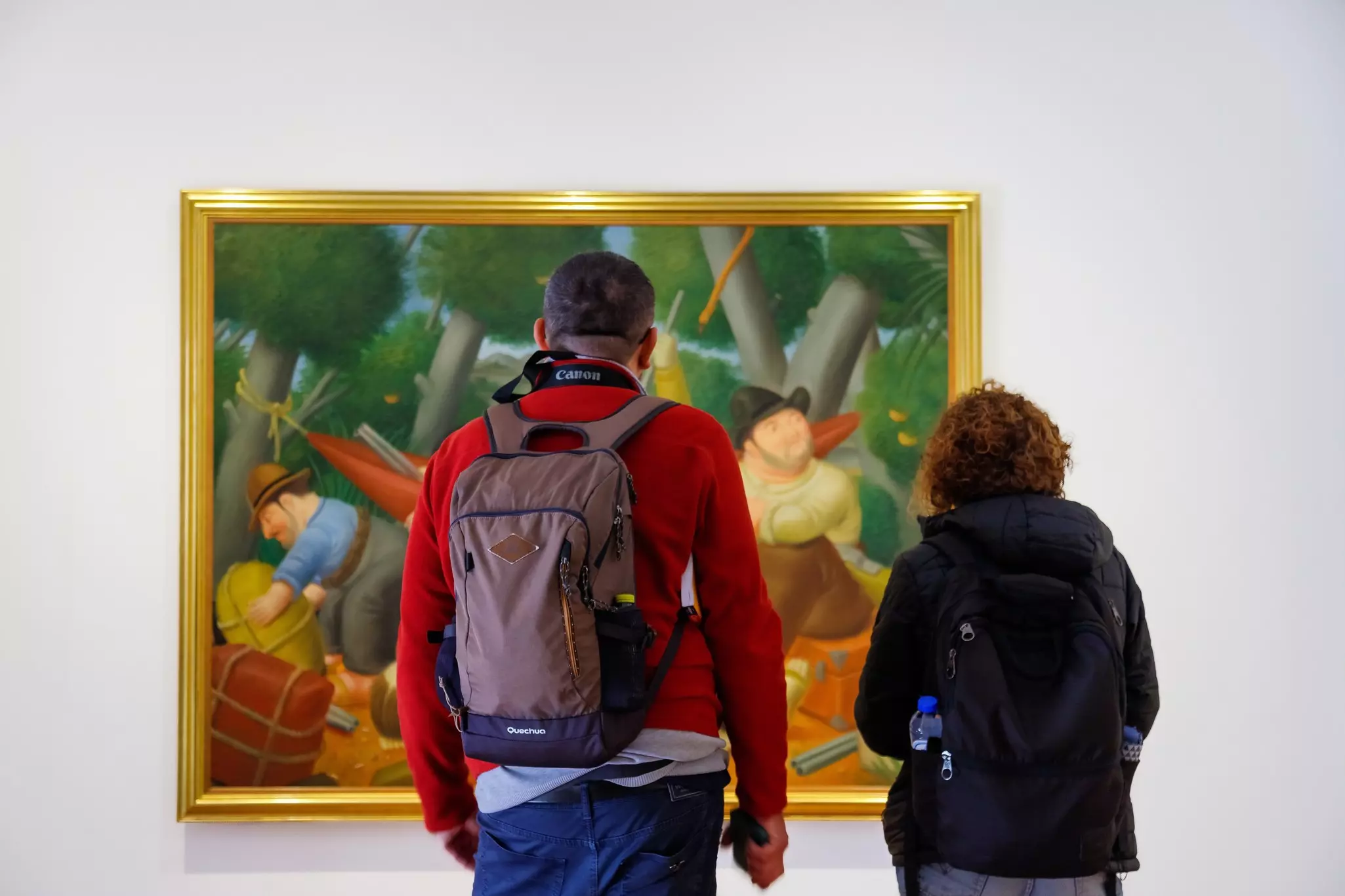 People looking at a colorful painting on a white wall.