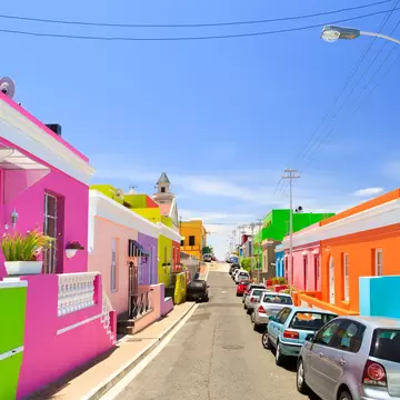 A series of row houses and front walls, each a bright pastel shade of pink, green, orange, yellow and red, flank either side of the street.