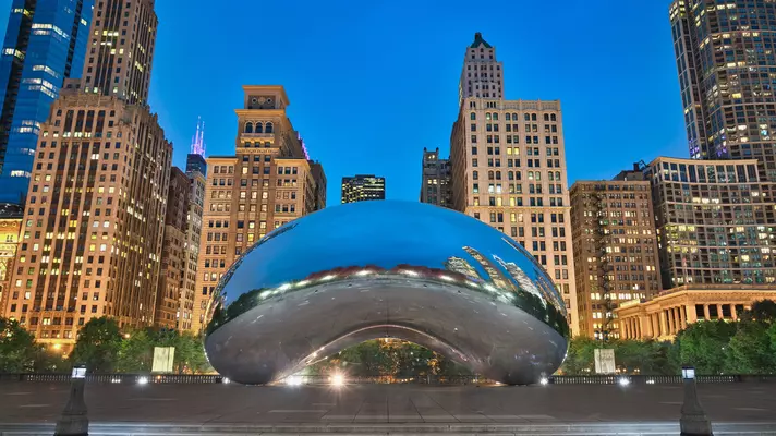 In a city park, a round sculpture with a mirrored surface reflects the skyline around it.