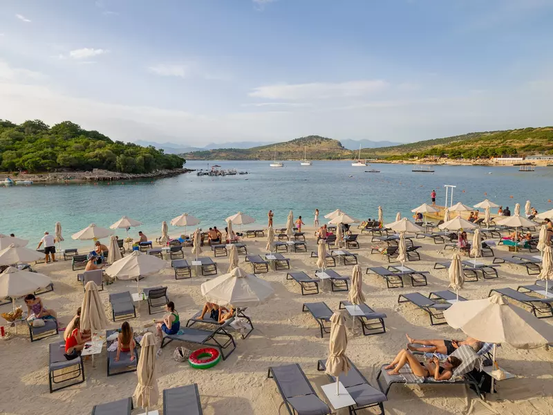 whit beach umbrellas in front of water with sailboats