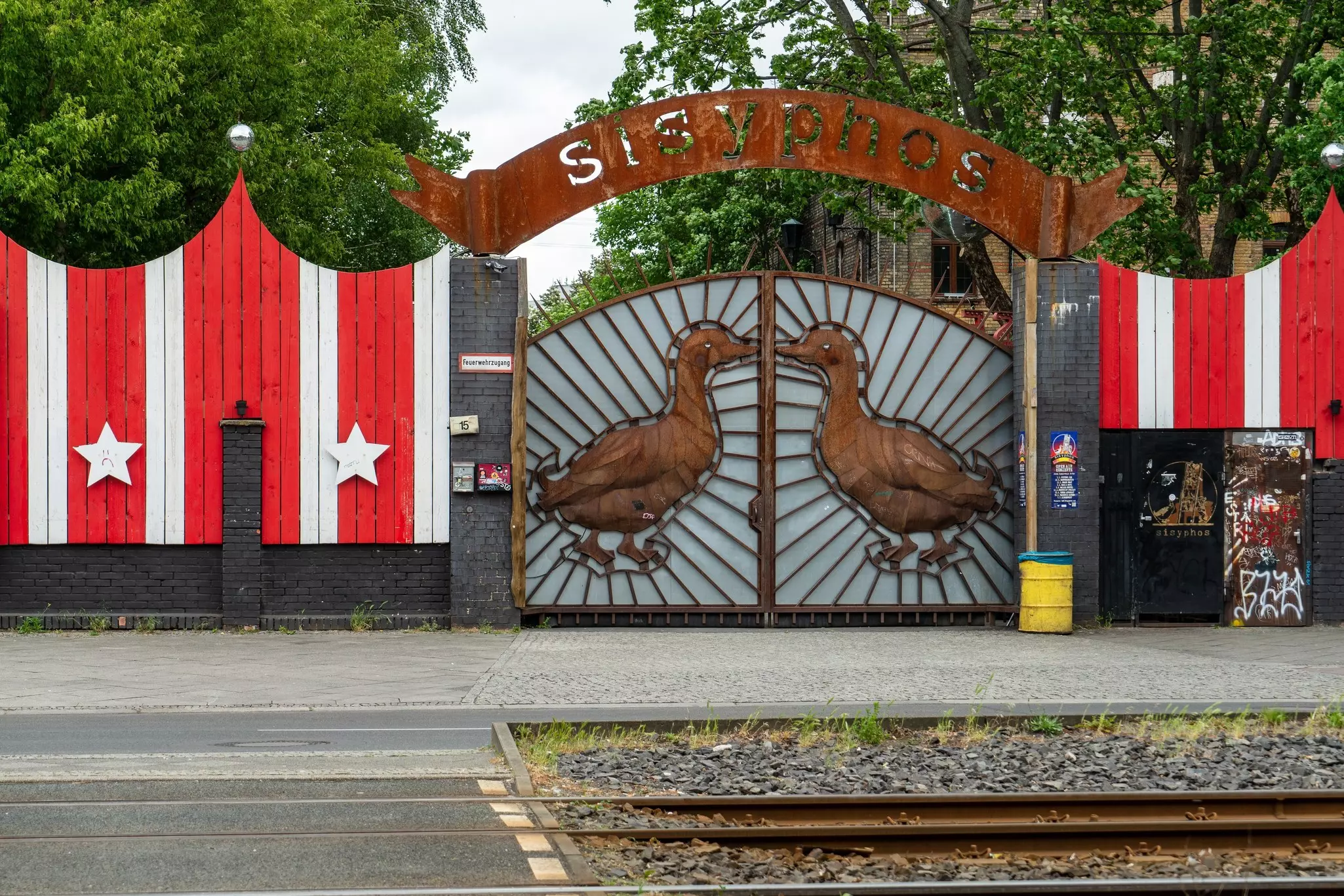 The exterior of a nightclub with a large sign over its entry gates that says "Sisyphos". The gates are decorated with two large ducks