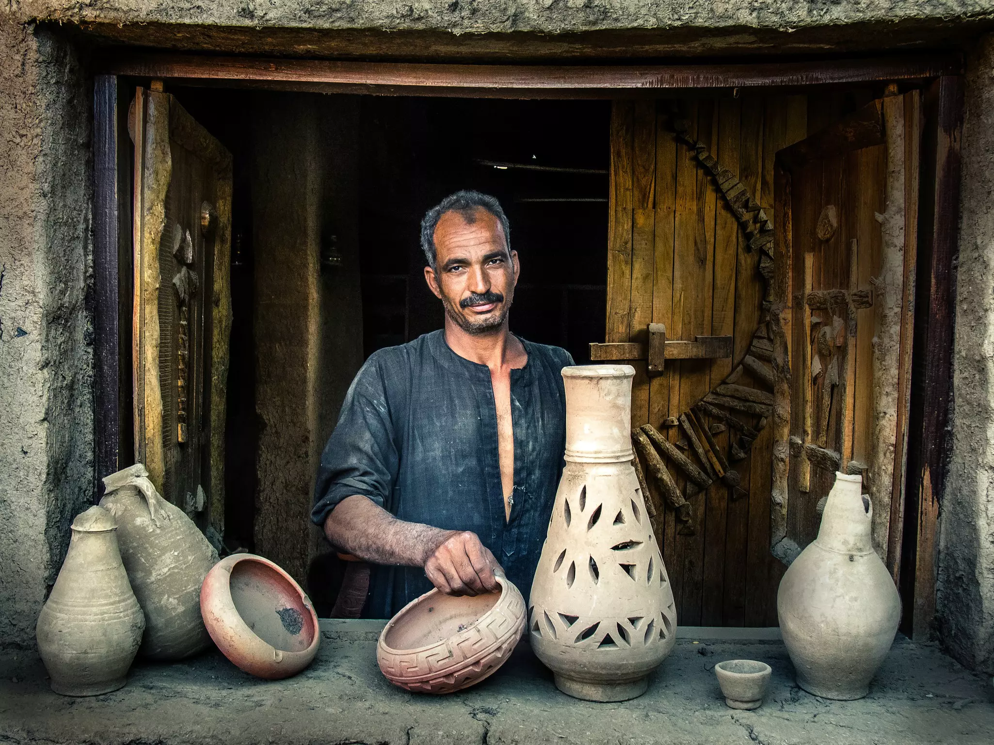 A man standing on a window showing pottery products in Luxor, Egypt.