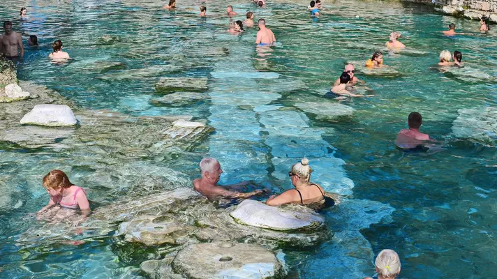 A group of people swim in a thermal spring with clear blue water. 