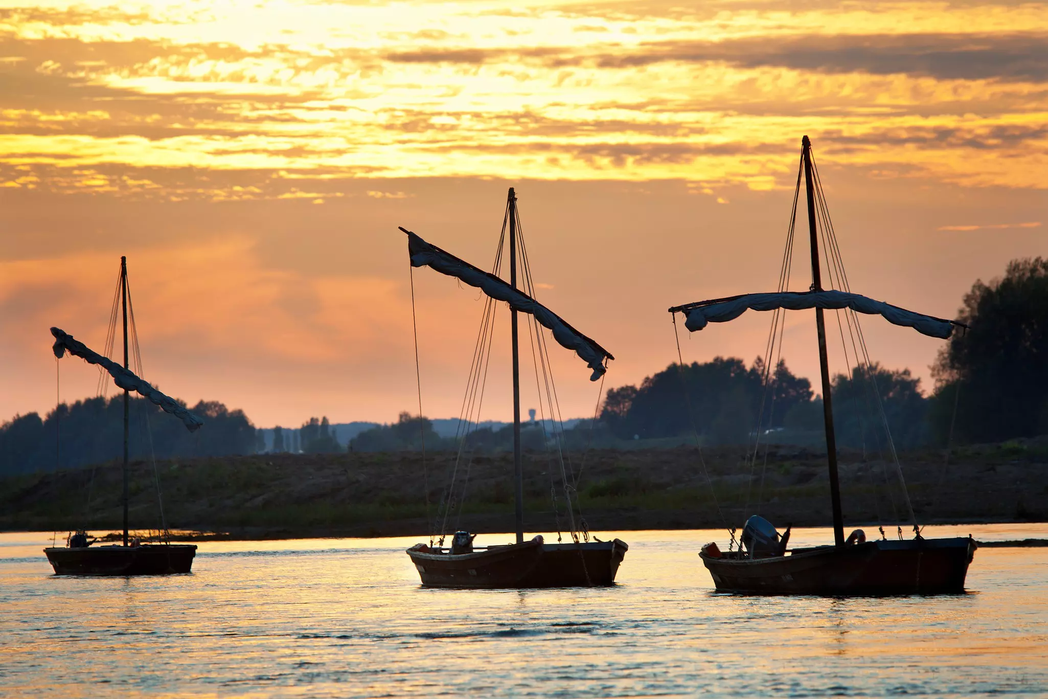 Traditional fishing boats with sails are moored in a river at sunset.